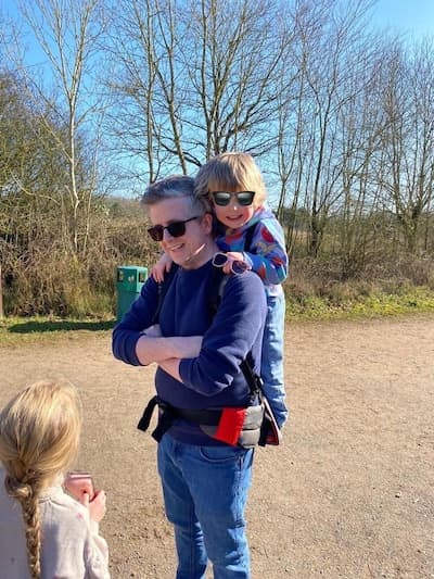 Customer Photo of a parent carrying a child with the Step Caddy child carrier - both smiling broadly. Step Caddy toddler carrier for outdoor adventures with kids, perfect for hiking and family outings.