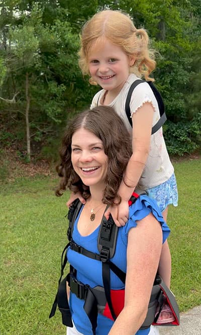 Mother carrying daughter with Step Caddy child carrier.