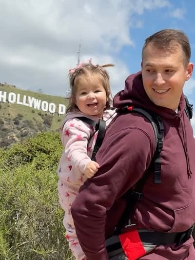 Customer Photo of a parent carrying a child with the Step Caddy child carrier - both smiling broadly. Step Caddy toddler carrier for outdoor adventures with kids, perfect for hiking and family outings.