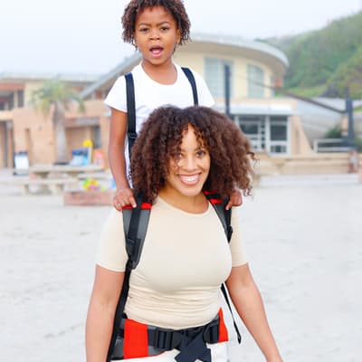 Picture of a parent carrying their child with Step Caddy child carrier - both smiling broadly. Step Caddy toddler carrier for outdoor adventures with kids, perfect for hiking and family outings.