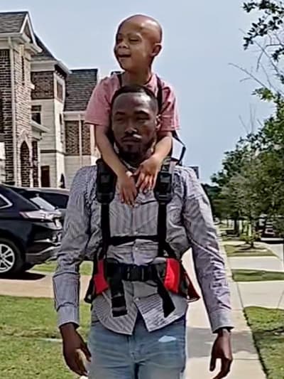 Customer Photo of a parent carrying a child with the Step Caddy child carrier - both smiling broadly. Step Caddy toddler carrier for outdoor adventures with kids, perfect for hiking and family outings.