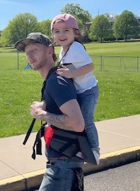 Customer Photo of a parent carrying a child with the Step Caddy child carrier - both smiling broadly. Step Caddy toddler carrier for outdoor adventures with kids, perfect for hiking and family outings.