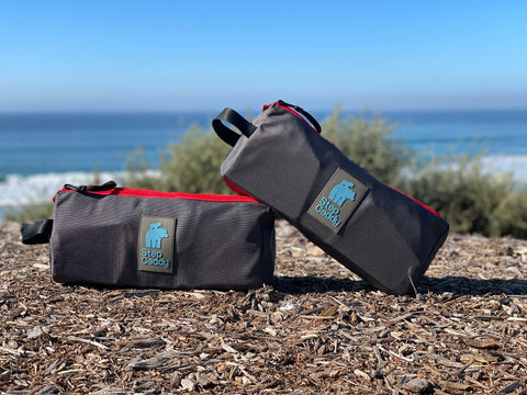 Two stacked Step Caddy travel bags on a beach with the ocean in the background